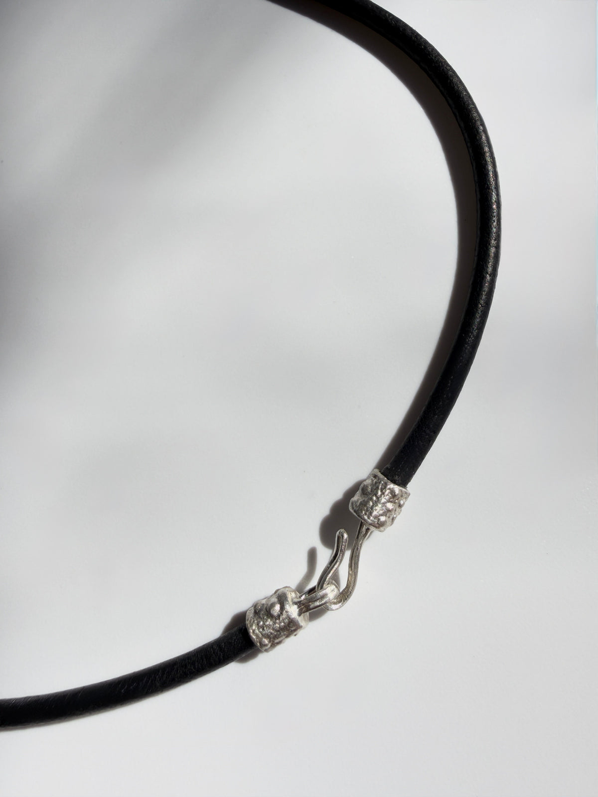 Clasp detail of the Thalassa Urchin Necklace showing the sterling silver hook closure on a black leather cord