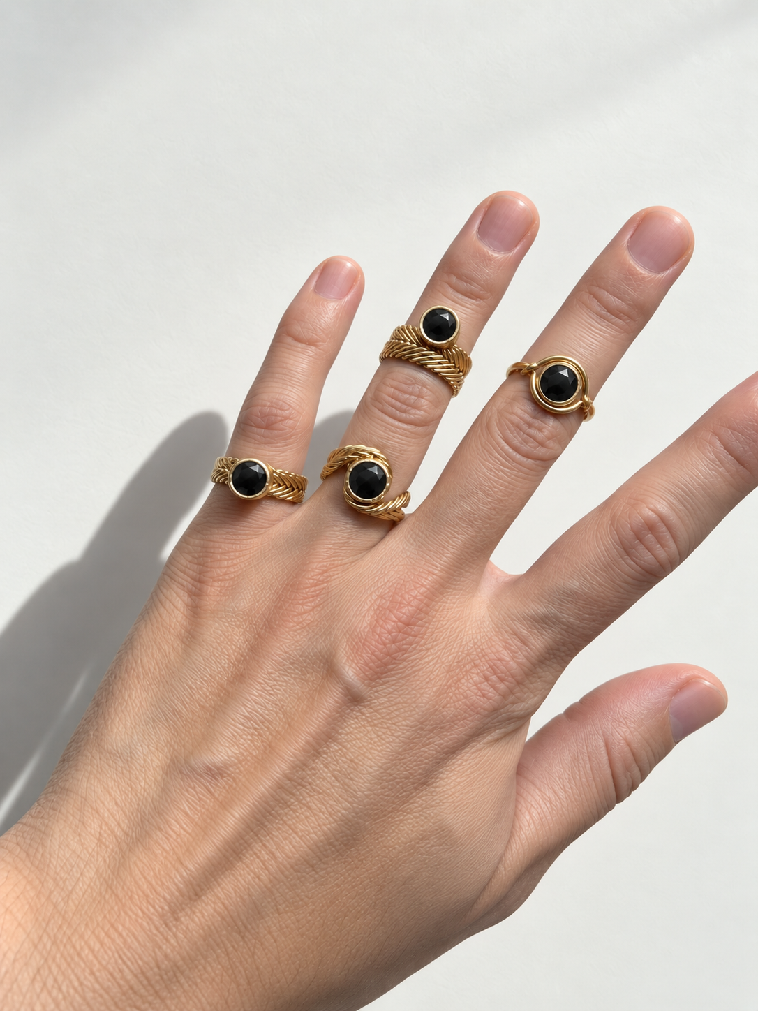 A hand wearing five gold rings with round black stones, photographed against a clean white background with a soft shadow.