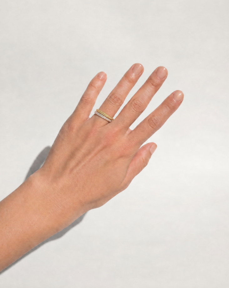 A hand wearing two stacked Hygeia Woven Rings, one gold vermeil and one sterling silver, showing the narrow handwoven band on the finger